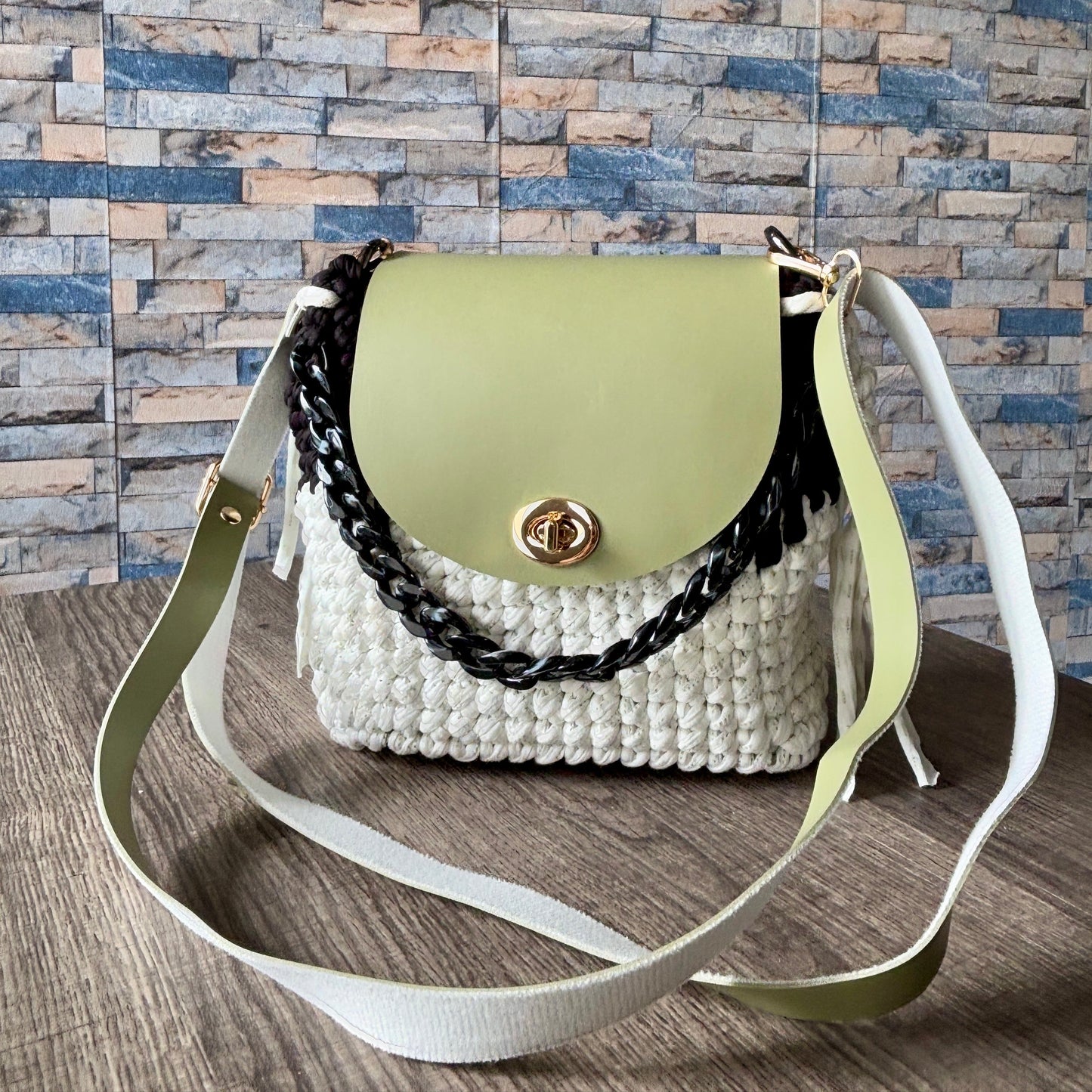 Green handbag with a textured white base and black chain detail 